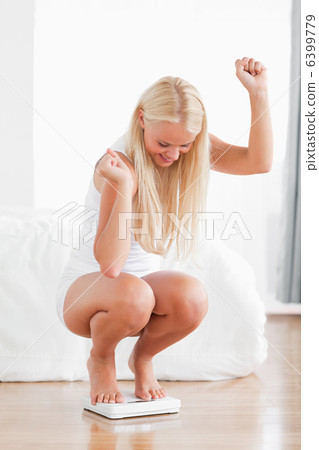 Portrait of a sportive woman squatting on a weighing machine 6399779