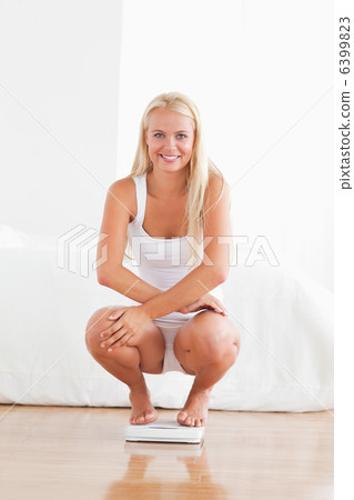 Portrait of a woman squatting on a weighing machine Portrait of a woman squatting on a weighing machine 6399823