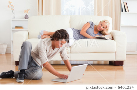 Man using a laptop while his girlfriend is holding a book Man using a laptop while his girlfriend is holding a book 6401224