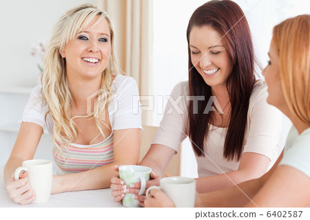 Laughing young Women sitting at a table with cups 6402587