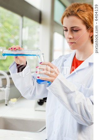 Portrait of a red-haired scientist pouring liquid Portrait of a red-haired scientist pouring liquid 6404139