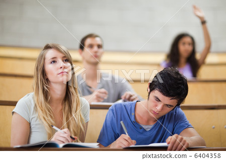 Students taking notes while their classmate is raising her hand 6404358