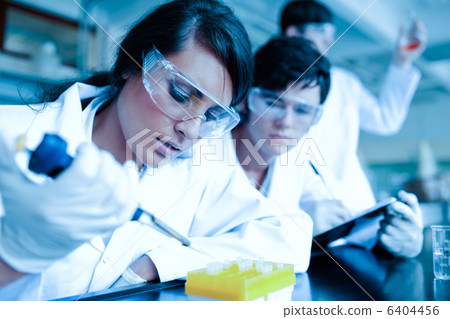 Young scientist dropping liquid in test tubes while her partner is taking notes Young scientist dropping liquid in test tubes while her partner is taking notes 6404456