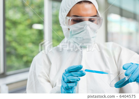 Protected female science student dropping blue liquid in a Petri 6404575