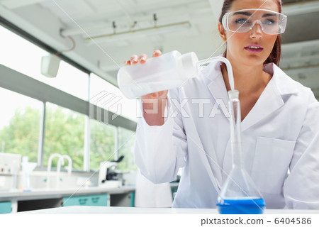 Female science student pouring liquid with protective glasses Female science student pouring liquid with protective glasses 6404586