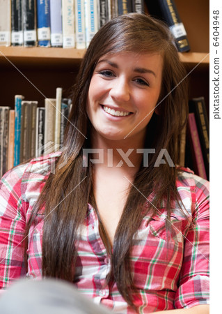 Portrait of a smiling student sitting against shelves Portrait of a smiling student sitting against shelves 6404948