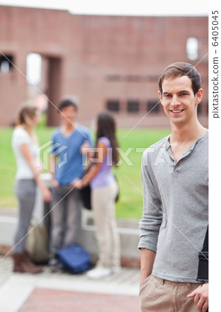 Portrait of a male student posing while his classmates are talking Portrait of a male student posing while his classmates are talking 6405045
