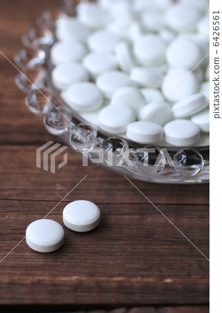 White pills in a glass dish and two tablets of medicine 6426561