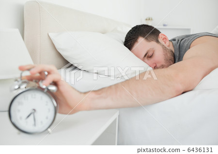 Sleeping handsome man being awakened by an alarm clock 6436131