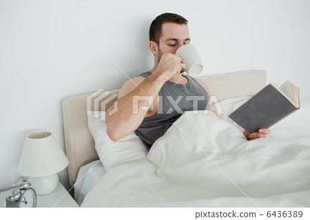 Smiling man reading a novel while drinking a coffee Smiling man reading a novel while drinking a coffee 6436389