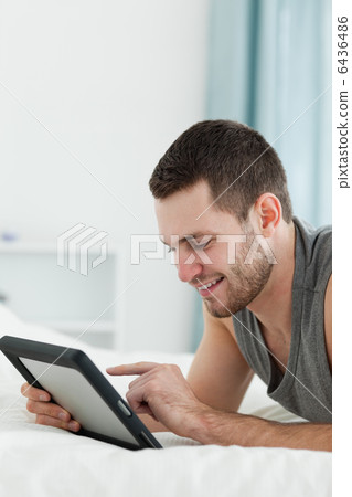 Portrait of a smiling man using a tablet computer while lying on Portrait of a smiling man using a tablet computer while lying on 6436486