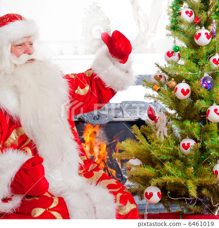 Santa sitting at the Christmas tree, near fireplace and looking Santa sitting at the Christmas tree, near fireplace and looking 6461019