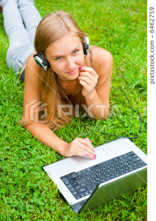 A smiling young girl with laptop outdoors listening music by hea A smiling young girl with laptop outdoors listening music by hea 6462759