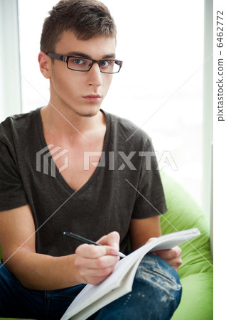 Young adult man writing in his copybook while sitting on a large Young adult man writing in his copybook while sitting on a large 6462772