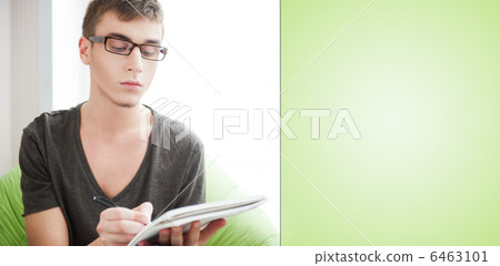 Young adult man writing in his copybook while sitting on a large 6463101