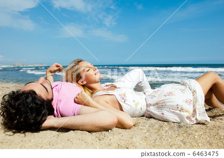 Young couple lying together on a sand by sea and looking to a sk Young couple lying together on a sand by sea and looking to a sk 6463475