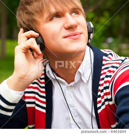 Student outside sitting on green grass and listening music via h Student outside sitting on green grass and listening music via h 6463804