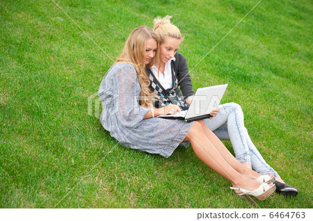 Portrait of two smiling women using laptop on a green meadow at Portrait of two smiling women using laptop on a green meadow at 6464763