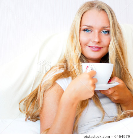 Smiling woman drinking a coffee lying on a bed at home or hotel. 6464979
