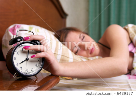 Young sleeping female turns alarm clock off Young sleeping female turns alarm clock off 6489157