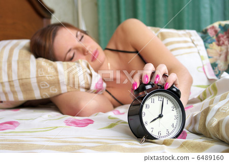 Young sleeping female turns alarm clock off 6489160