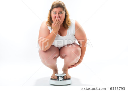 Obese young woman crouching on a scale 6538793