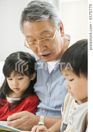 Grandfather and grandchildren reading a picture book in the living room Grandfather and grandchildren reading a picture book in the living room 6570779