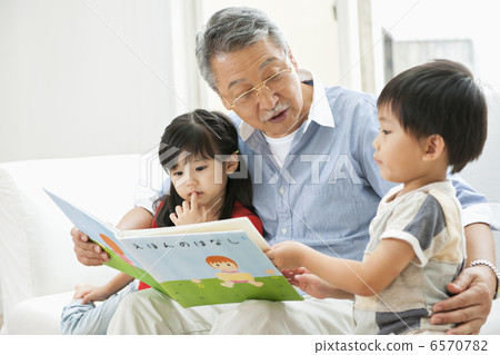Grandfather and grandchildren reading a picture book in the living room 6570782