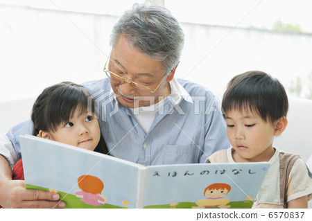 Grandfather and grandchildren reading a picture book in the living room 6570837