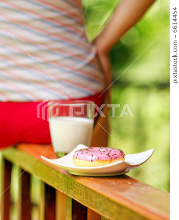 Young woman sitting on terrace with milk and donut Young woman sitting on terrace with milk and donut 6614454