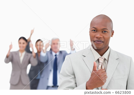 Businessman with cheering team behind him giving thumb up 6623800