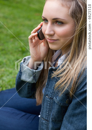 Young blonde woman calling with her mobile phone while sitting i Young blonde woman calling with her mobile phone while sitting i 6625518