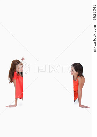 Teenage girls looking at each other in front of a blank poster 6626041
