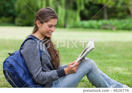 Young relaxed woman sitting on the grass while reading a book 6626776