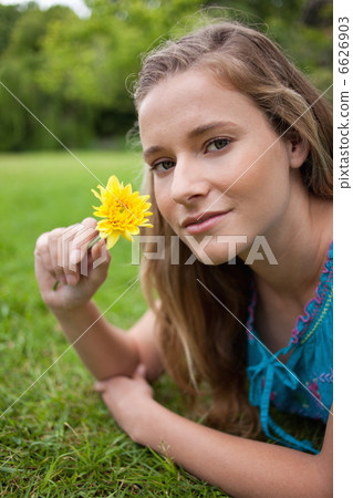 Young relaxed girl lying on the grass in a park while holding a 6626903