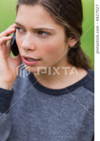 Young serious girl talking on the phone while looking towards th 6627027