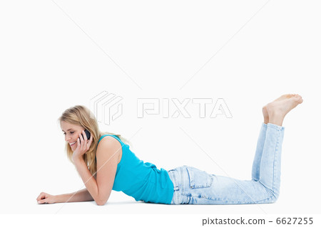 A young woman is talking on her mobile phone while lying on the 6627255