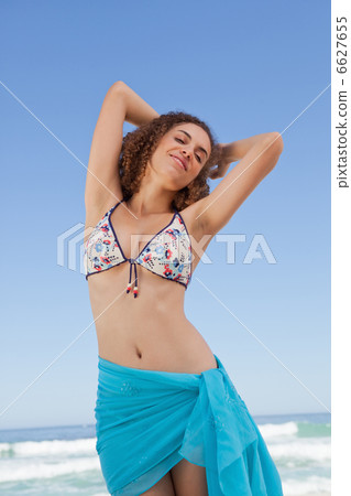 Young woman standing in front of the sea while showing her welln Young woman standing in front of the sea while showing her welln 6627655