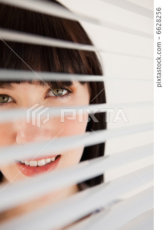 A woman looking forward through her blinds without moving them 6628256