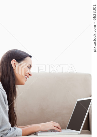 A laughing woman lying on her couch with her laptop 6628301