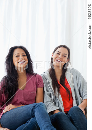 Two laughing women on the couch as they look straight ahead Two laughing women on the couch as they look straight ahead 6628308