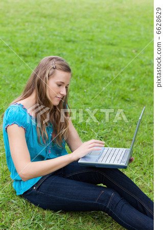 Young relaxed woman using her laptop while sitting on the grass 6628629