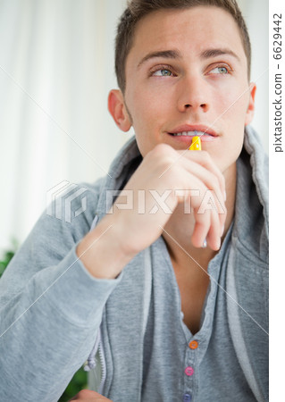 Close-up of a smiling student chewing his pencil Close-up of a smiling student chewing his pencil 6629442