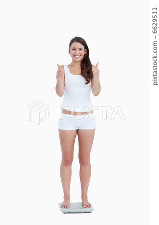 Smiling woman placing her thumbs up while standing on weighing s Smiling woman placing her thumbs up while standing on weighing s 6629511