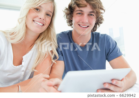 A smiling couple holding a tablet and looking at the camera A smiling couple holding a tablet and looking at the camera 6629942