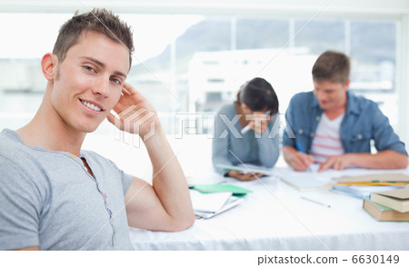 A smirking student sits in front of his friends as he looks into 6630149