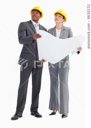Businessman and woman wearing hard hats holding paper looking up 6630152