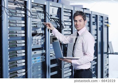 businessman with laptop in network server room 6641019