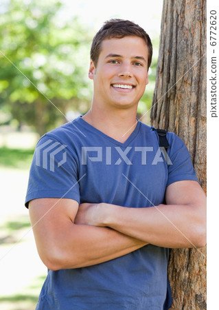 Close-up of a smiling young man leaning against a tree Close-up of a smiling young man leaning against a tree 6772620