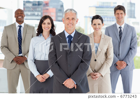 Mature smiling manager standing upright and followed by his team Mature smiling manager standing upright and followed by his team 6773243